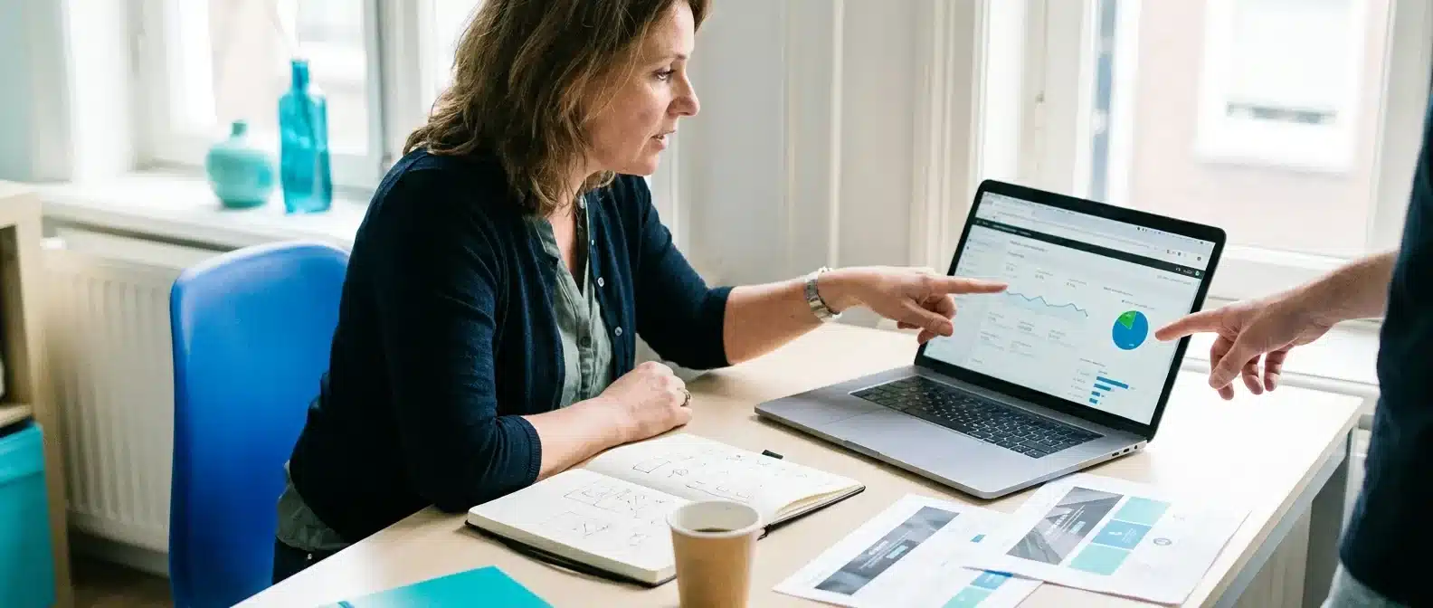 Ondernemer bespreekt analyticgegevens en conversiegrafieken op laptop met collega aan bureau.