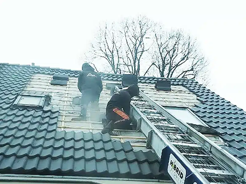 Dakdekkers van Dakwerk Nederland vervangen dakpannen op een woning, met een ladderlift langs het dak