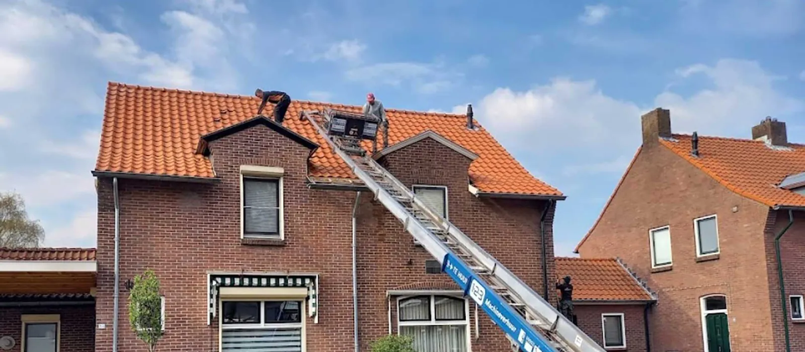Dakdekkers van Dakwerk Nederland aan het werk op een oranje pannendak, met een ladderlift tegen de gevel