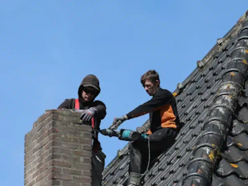 Twee dakdekkers van Dakwerk Nederland slopen een gemetselde schoorsteen op een pannendak
